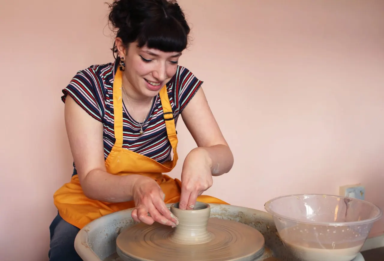 Woman in yellow apron shaping clay on a pottery wheel during a ceramics class.
