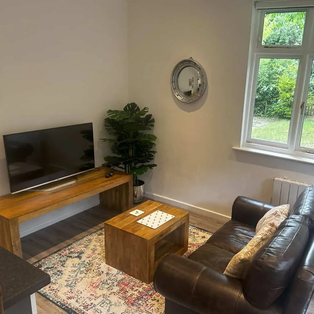 A comfortable lounge area with brown leather seating, wooden furniture, a television, potted plant and garden views through patio doors.