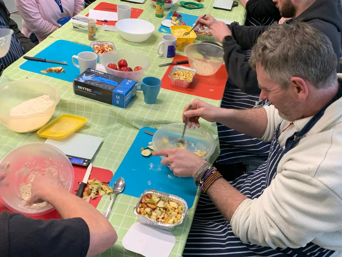 Adults and children preparing food together at a table with fresh ingredients and cooking utensils.