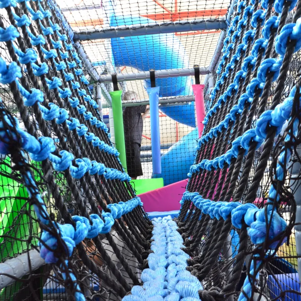 Interior view of a soft play facility with a rope climbing structure featuring blue rope netting and colourful padded supports.