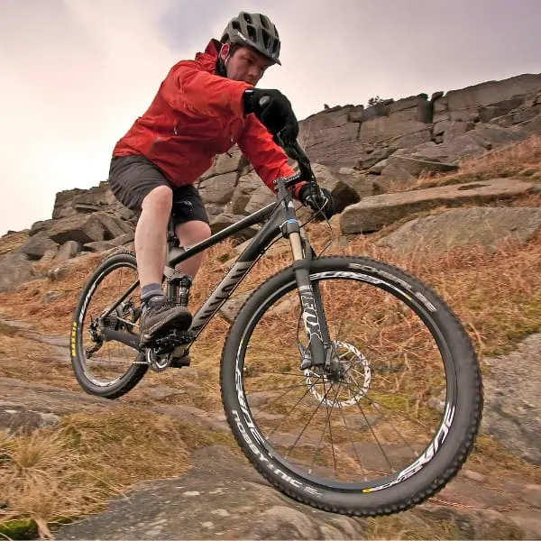 Cyclist in red jacket and helmet riding a mountain bike on rocky moorland terrain.