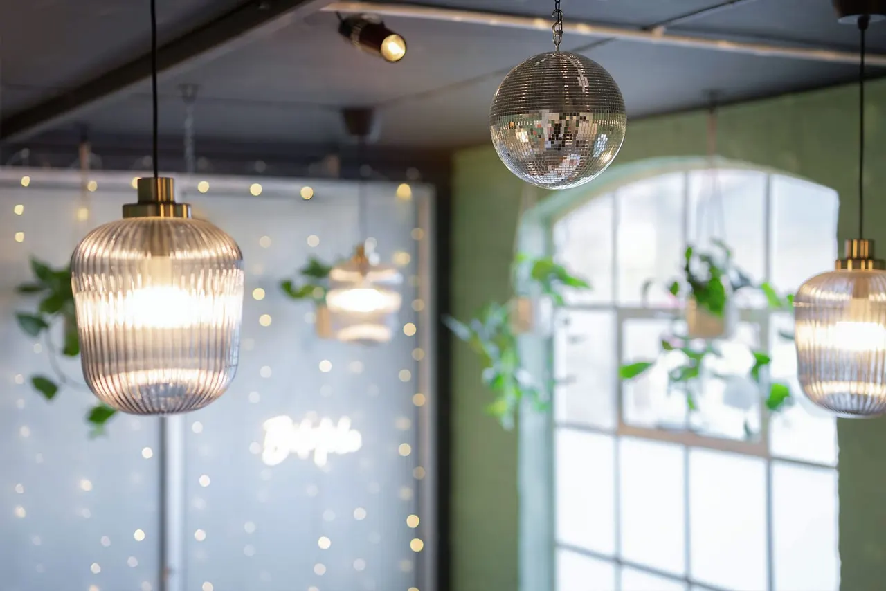 Modern interior with hanging pendant lights including a disco ball, potted plants, and large windows with natural light.