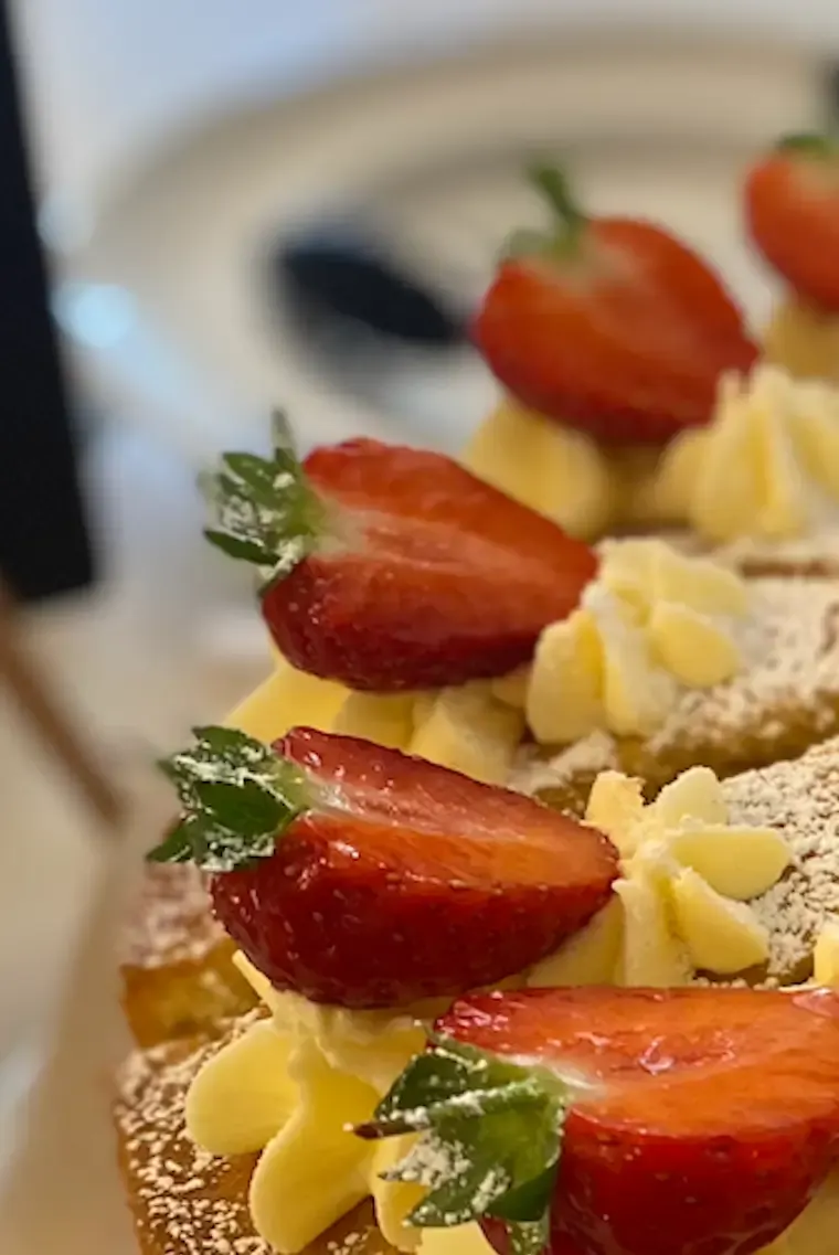 Close-up of a cake decorated with fresh strawberries and yellow piped cream on a pastry base.