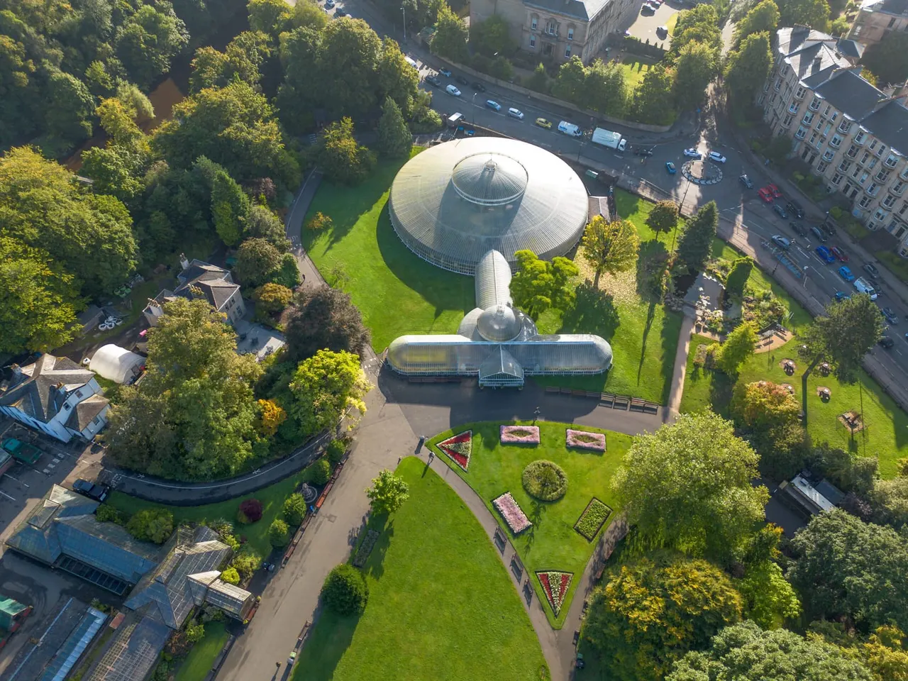 Aerial view of a distinctive domed greenhouse complex surrounded by manicured gardens and mature trees in an urban setting.