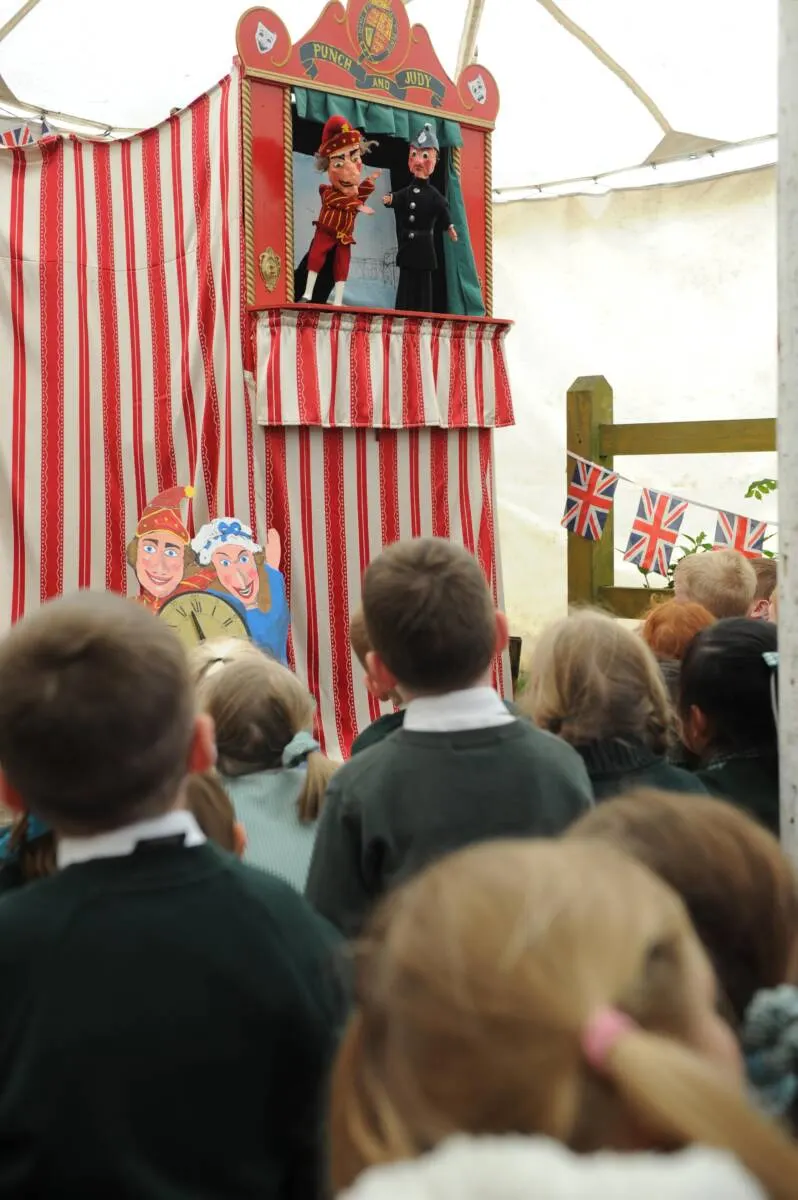 Children watching a traditional Punch and Judy puppet show booth with red and white striped canvas.