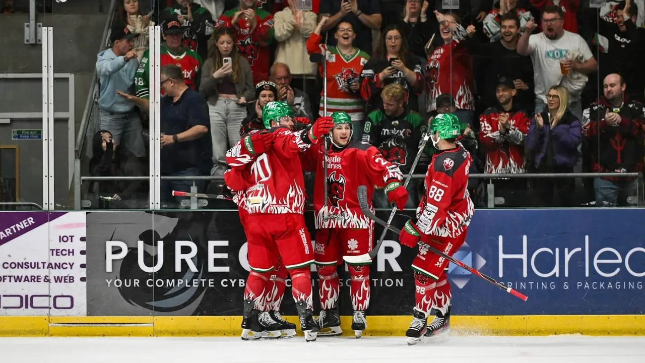 Ice hockey players in red flame jerseys celebrate with fans cheering in the stands behind the boards.