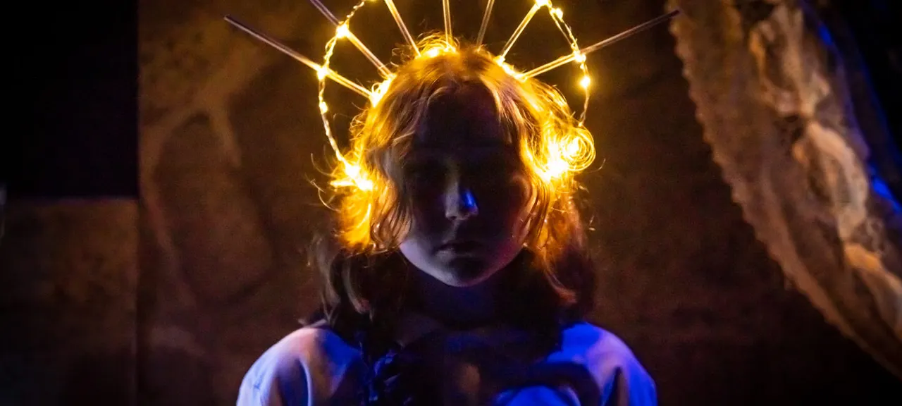 Person wearing illuminated golden light-up headpiece in dark stone setting at night.