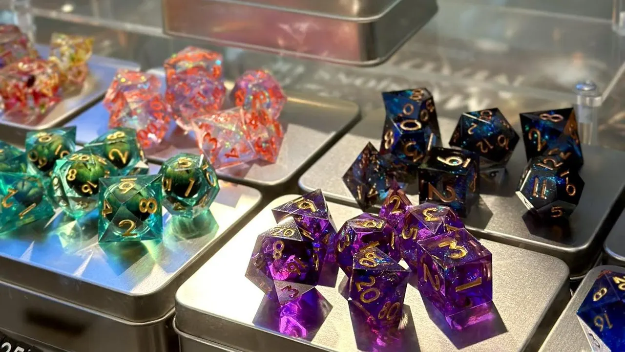 Colourful polyhedral dice sets in various colours displayed on white trays on a shop counter.