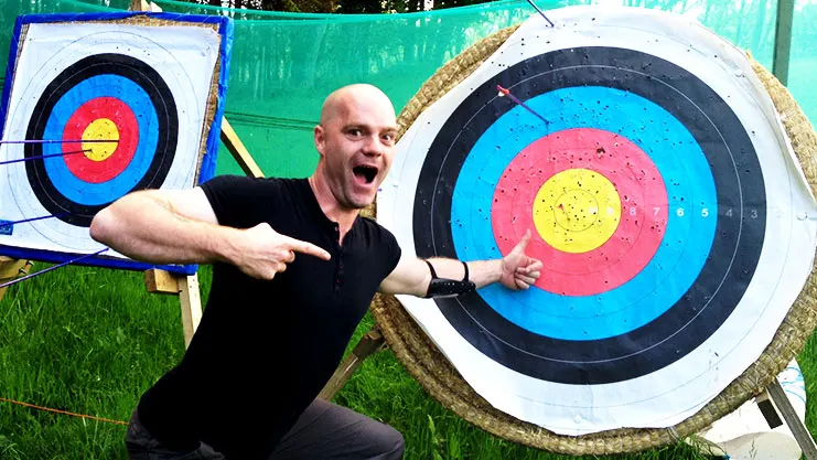 Man posing enthusiastically between two large colourful archery targets on grass.