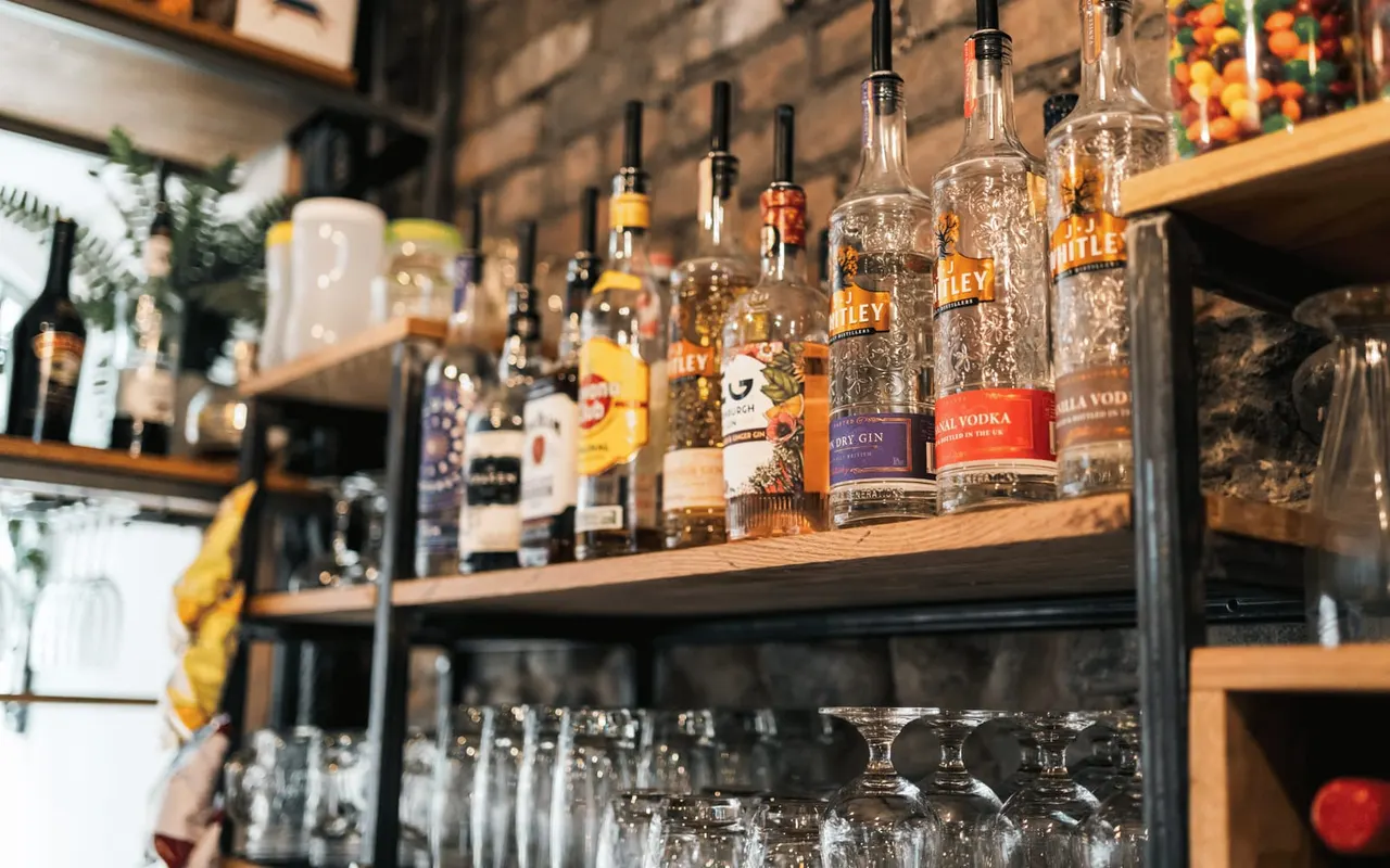 Bar shelves displaying various spirit bottles including gin and vodka, with glasses beneath.