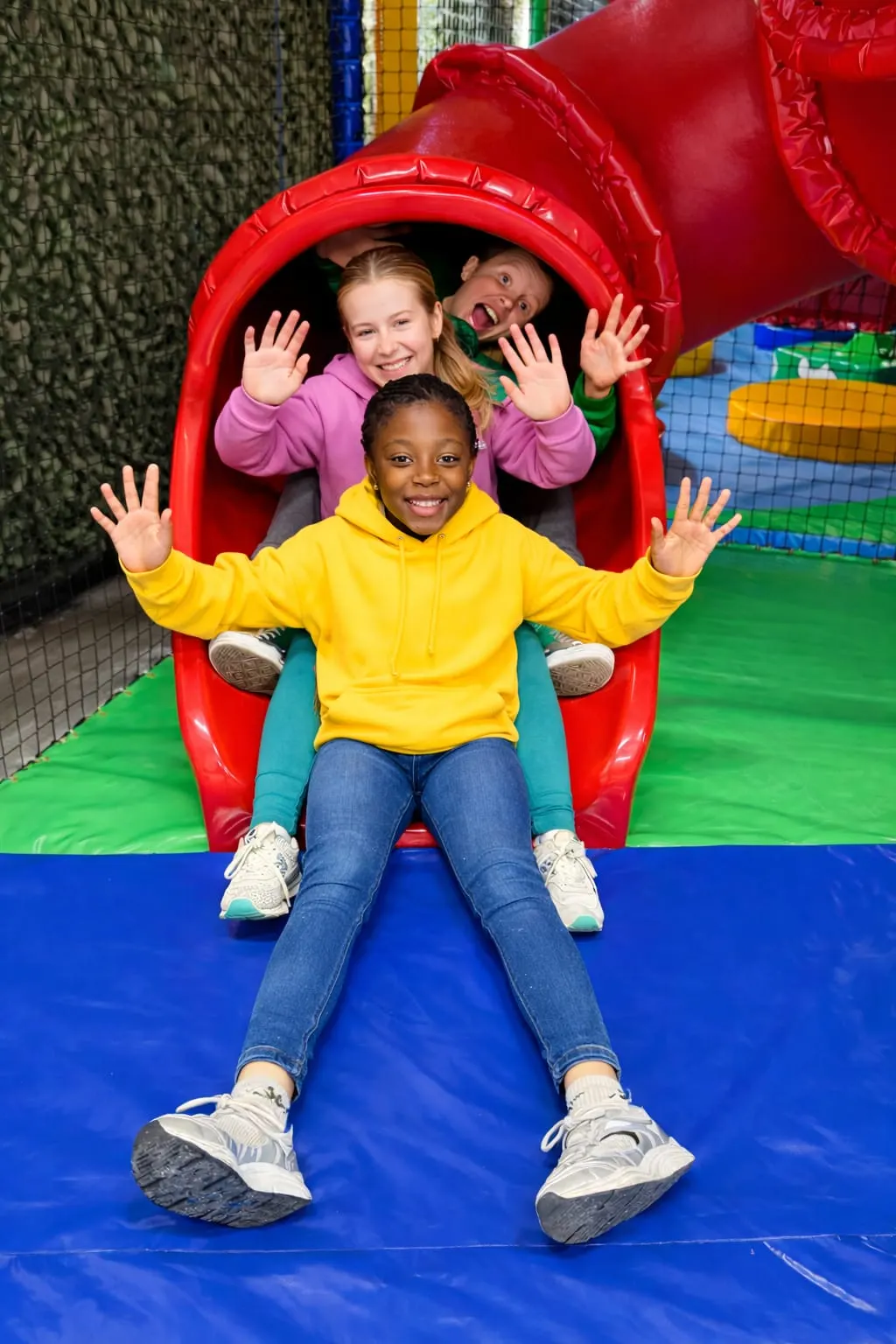 Three children enjoying a red inflatable slide at an indoor play centre.