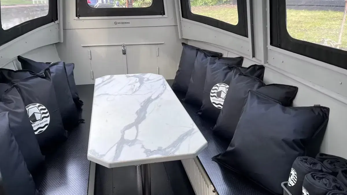 Interior of a boat cabin with a marble-effect table and black cushioned seating along both sides.