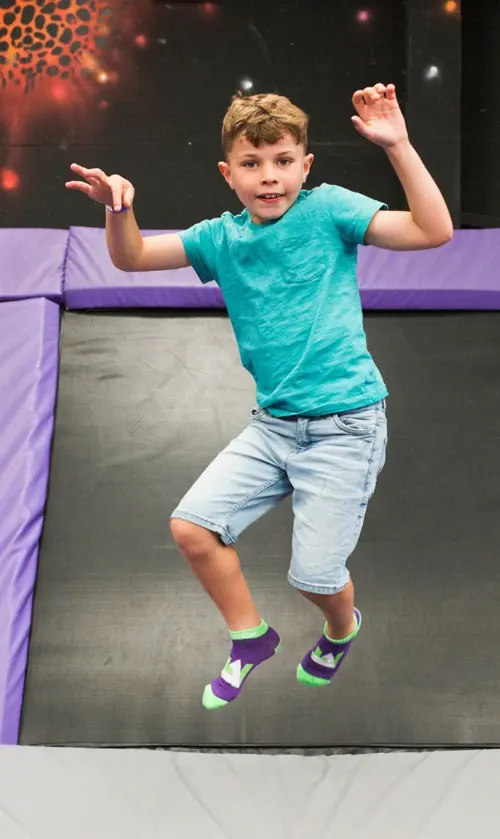 Young child jumping on a trampoline with arms raised, wearing a turquoise shirt and colourful socks.