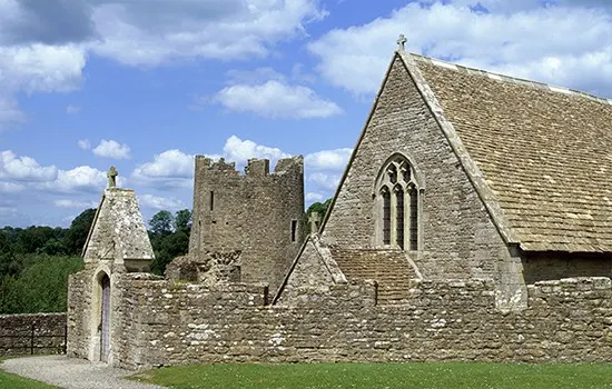 Historic stone castle ruins with crenellated tower and chapel against blue sky with white clouds.