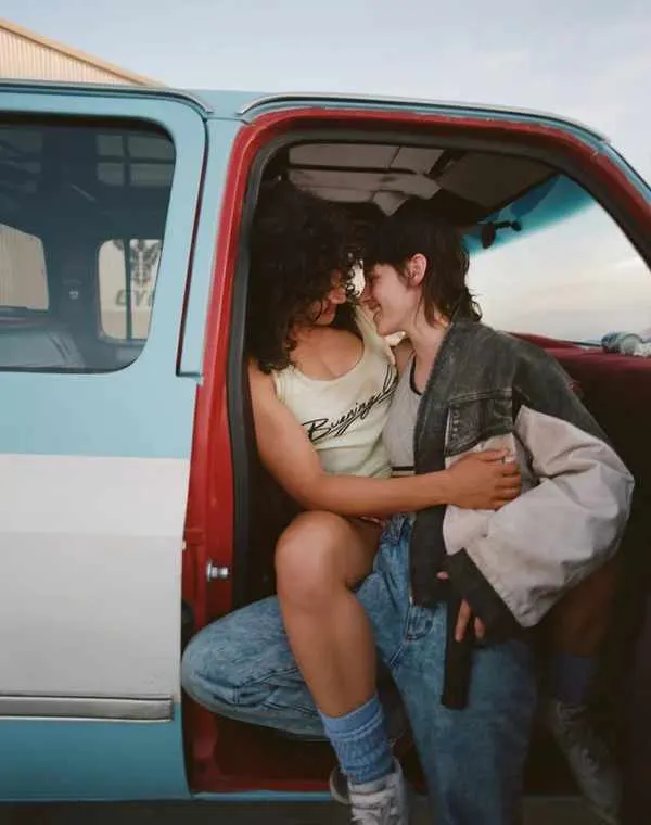 This is a PHOTOGRAPH, so here is the alt text:

Two young women sitting in the open passenger door of a red and turquoise vintage truck.