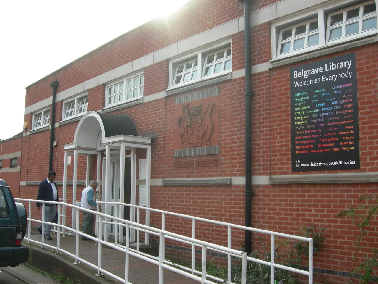 Red brick library building with entrance ramp and two people approaching the door marked "Belgrave Library Welcomes Everybody".