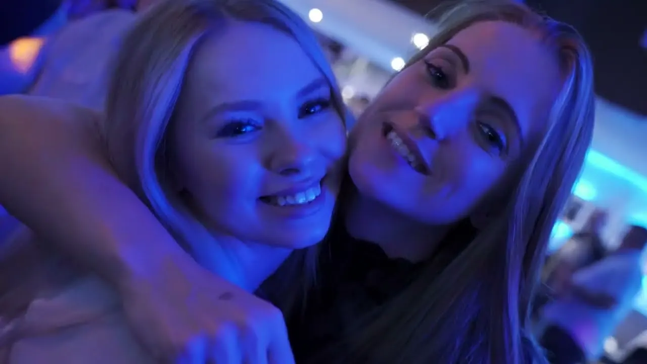 Two young women smiling at a nightclub with blue lighting.