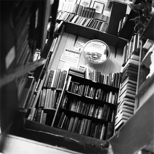 Overhead view of tall bookshelves stacked with books and vinyl records in a narrow shop interior.