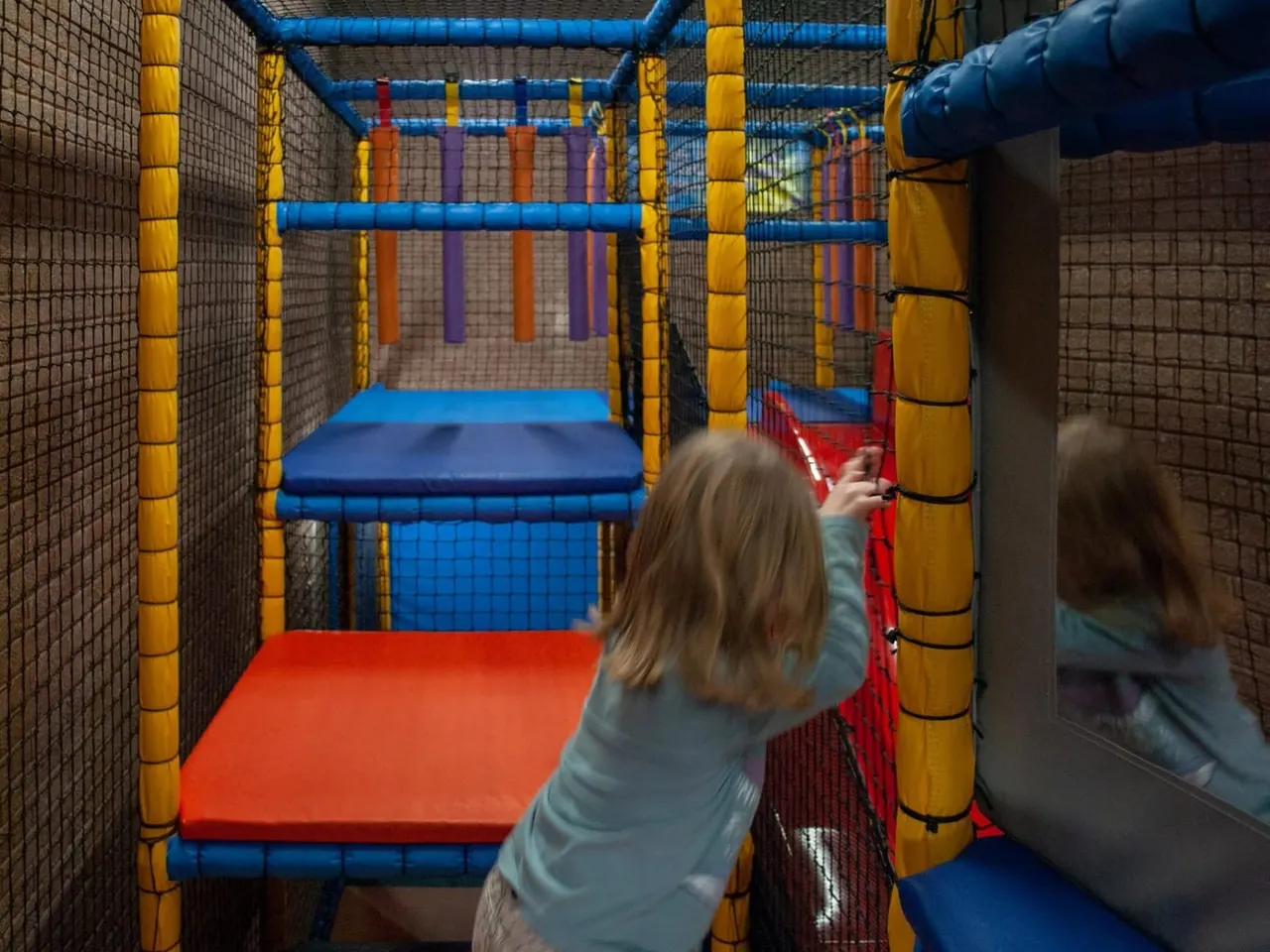 Children navigating through a colourful soft play structure with padded obstacles and tubes.