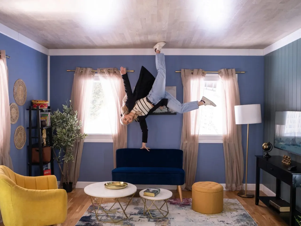 This is a designed graphic — a stylized promotional image with a person performing an inverted handstand pose superimposed over a living room interior.

GRAPHIC