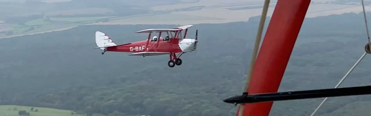 Two vintage biplane aircraft flying in formation over rural countryside and forests.