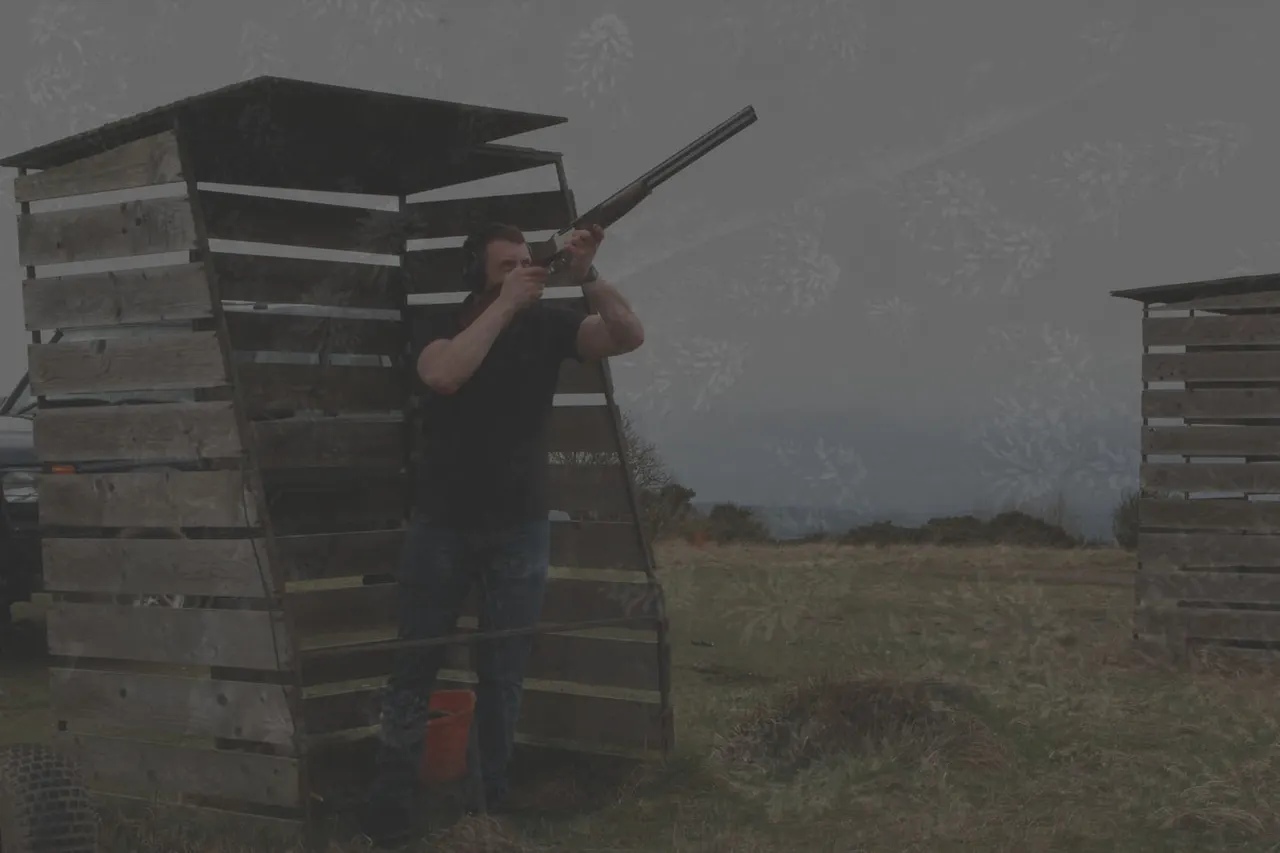 Man clay pigeon shooting at an outdoor range with wooden shooting stands in misty countryside.