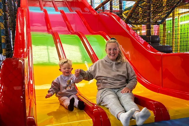 Two children sitting together on a colourful inflatable slide at an indoor play area.