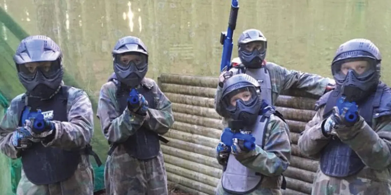 Group of paintball players in protective gear and masks holding paintball guns at an outdoor venue.