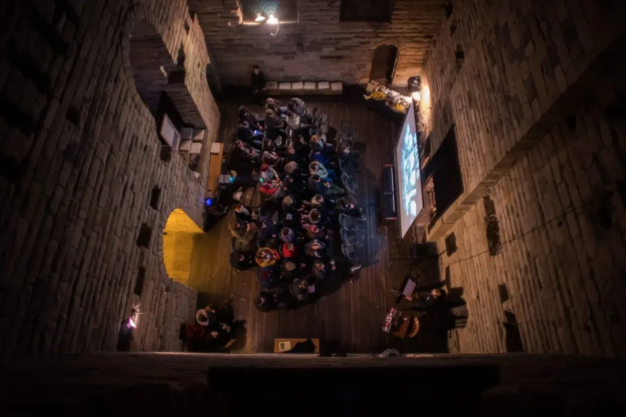 Overhead view of visitors gathered in a historic stone-walled castle chamber during an evening event or tour.