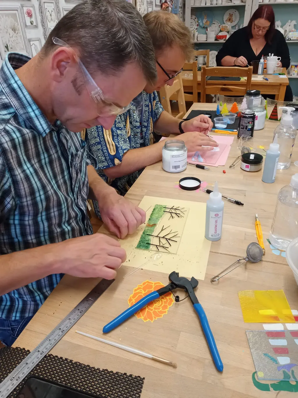 PHOTOGRAPH

Adults and children participating in a painting and craft workshop at a table with art supplies and materials.