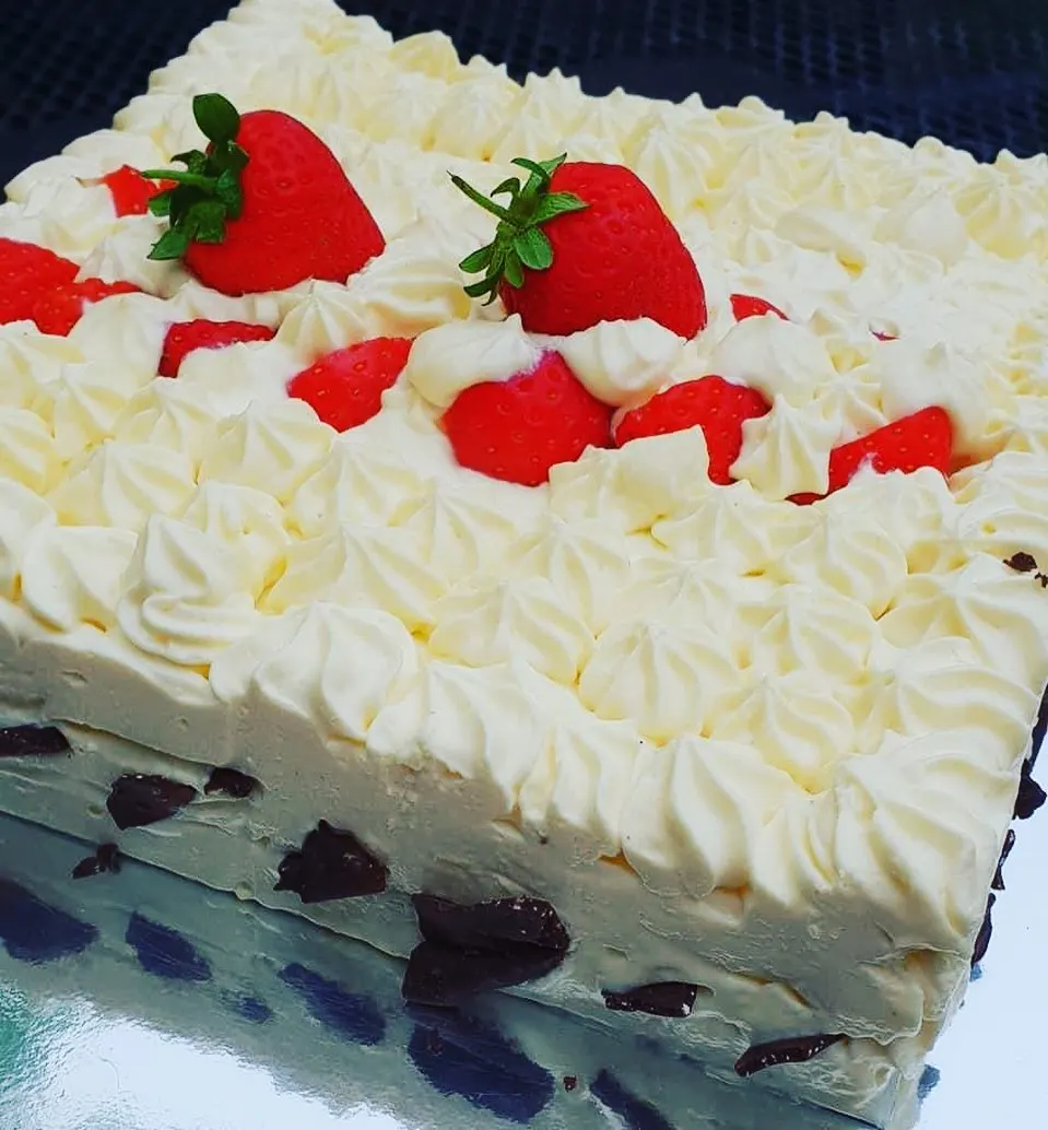 Cream layer cake decorated with piped frosting, fresh strawberries and dark berries.