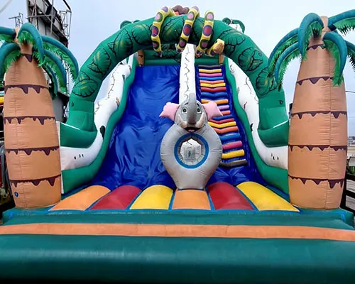 Large inflatable bouncy castle with green crocodile design and colorful sliding section.