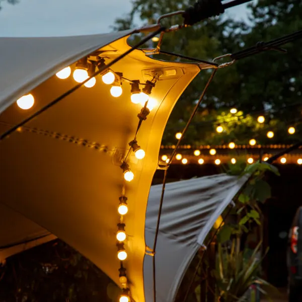 Illuminated yellow parasol with warm string lights at dusk in an outdoor garden setting.