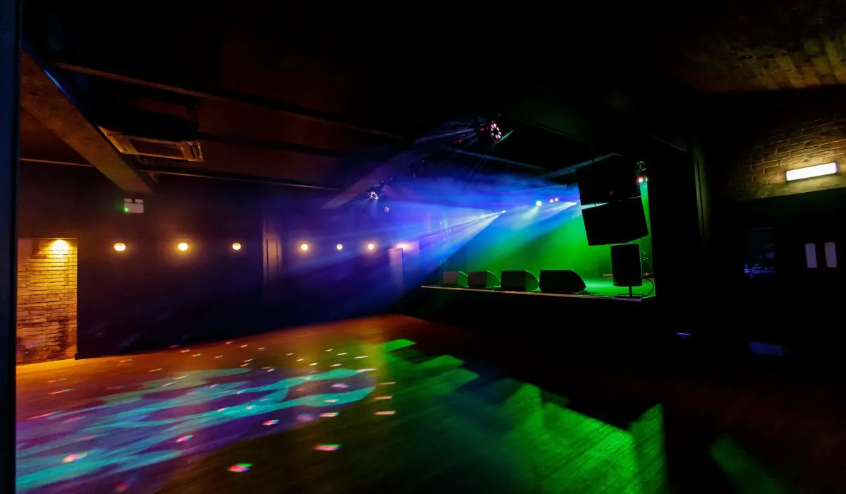 Empty nightclub dancefloor illuminated by colourful stage lighting and projection beams.