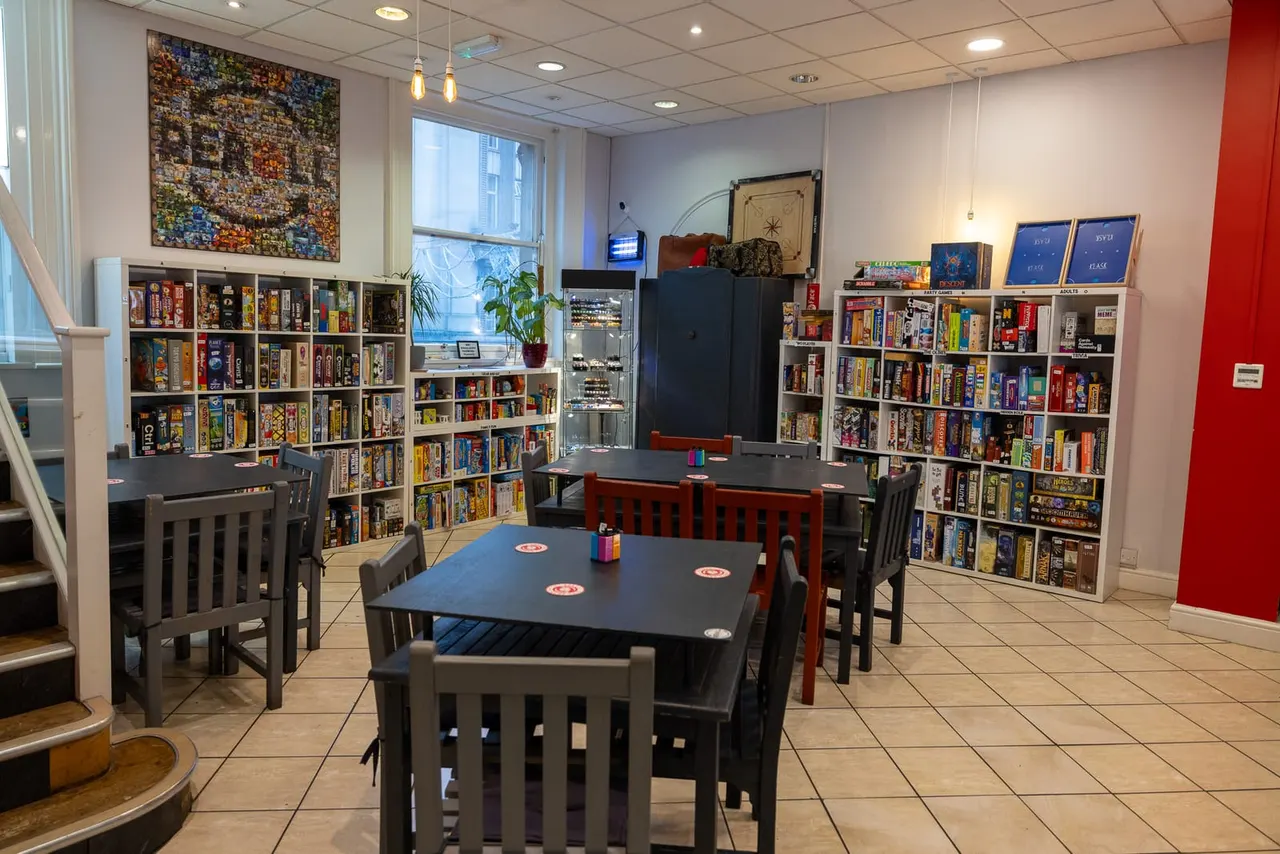 Interior of a board game café with multiple tables and chairs surrounded by shelves stocked with board games.