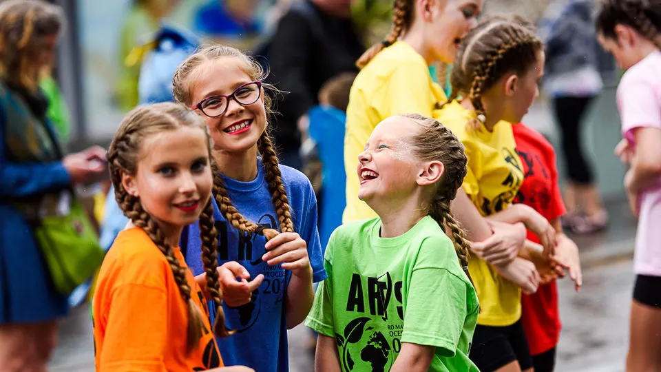 Children in brightly coloured t-shirts laughing and socialising together outdoors.