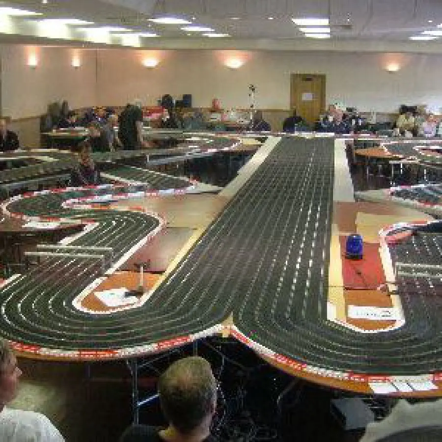 Visitors racing slot cars on multiple track layouts in an indoor racing hall.