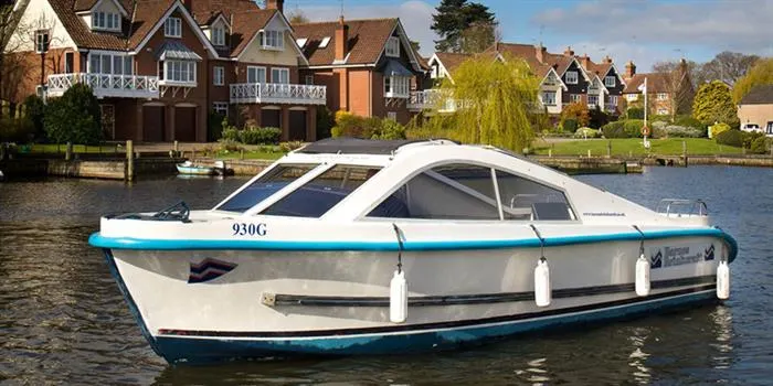 White and turquoise motorboat moored on a river in front of riverside residential buildings.