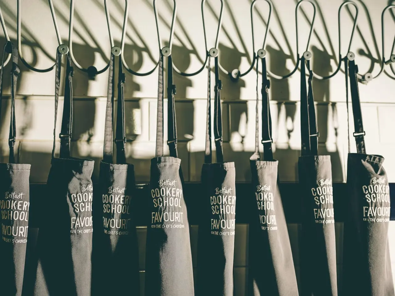 Row of branded aprons hanging on hooks against a white wall.