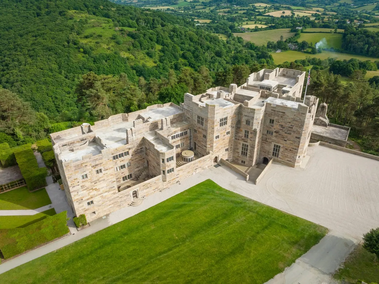 Aerial view of a large stone castle with manicured lawns surrounded by woodlands and rolling countryside.