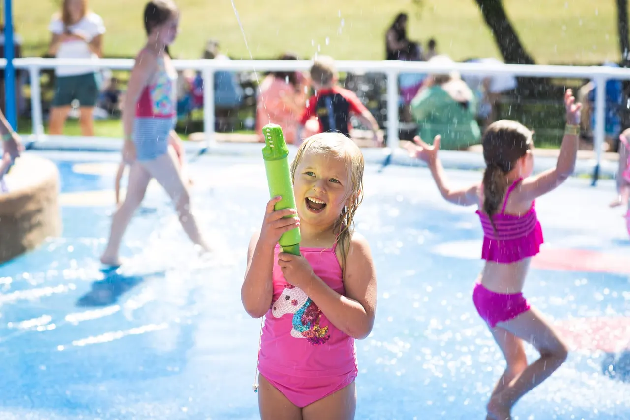 Young children playing with water toys in a shallow outdoor swimming pool on a sunny day.