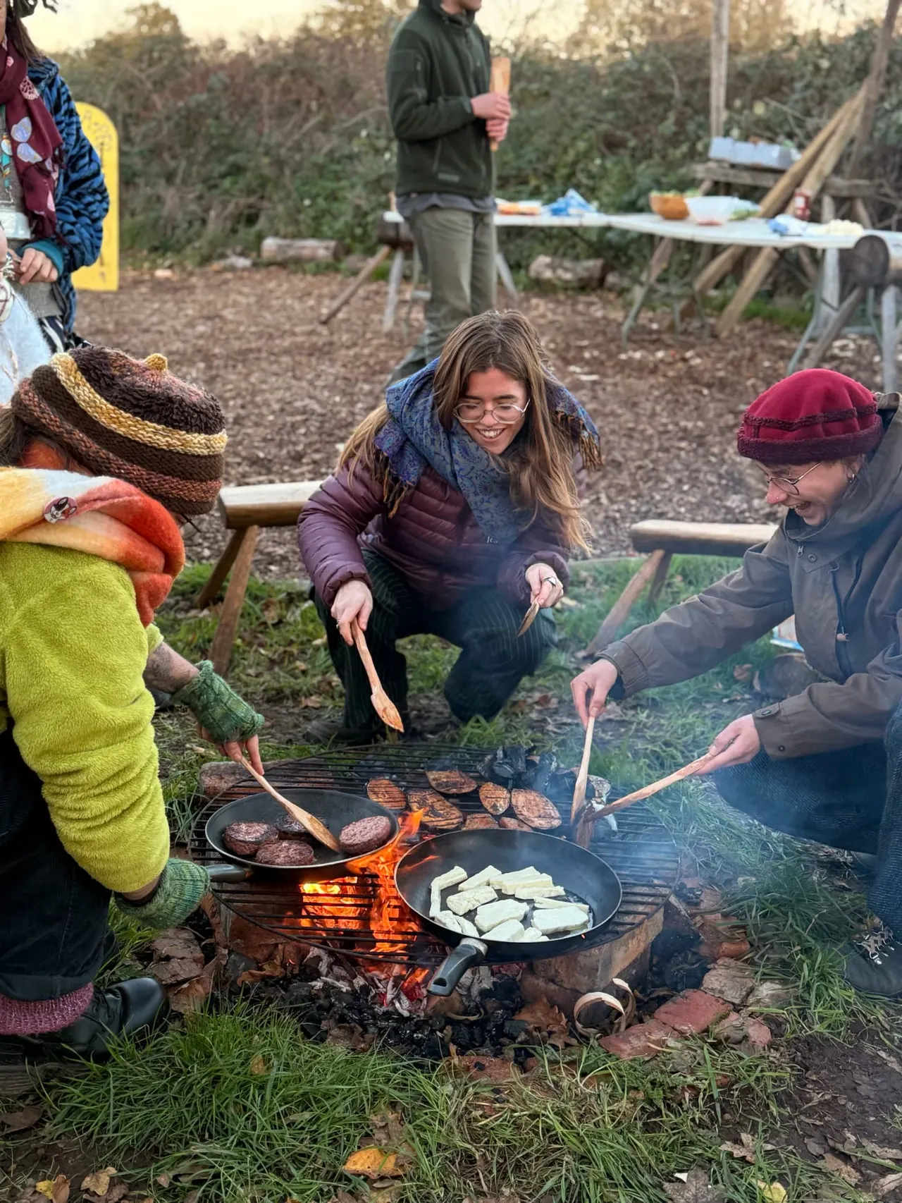 Group of visitors cooking food on a campfire grill in a woodland setting.