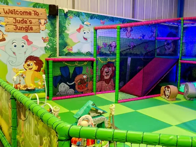 A jungle-themed children's soft play area with colourful climbing structures, slides, and netting.