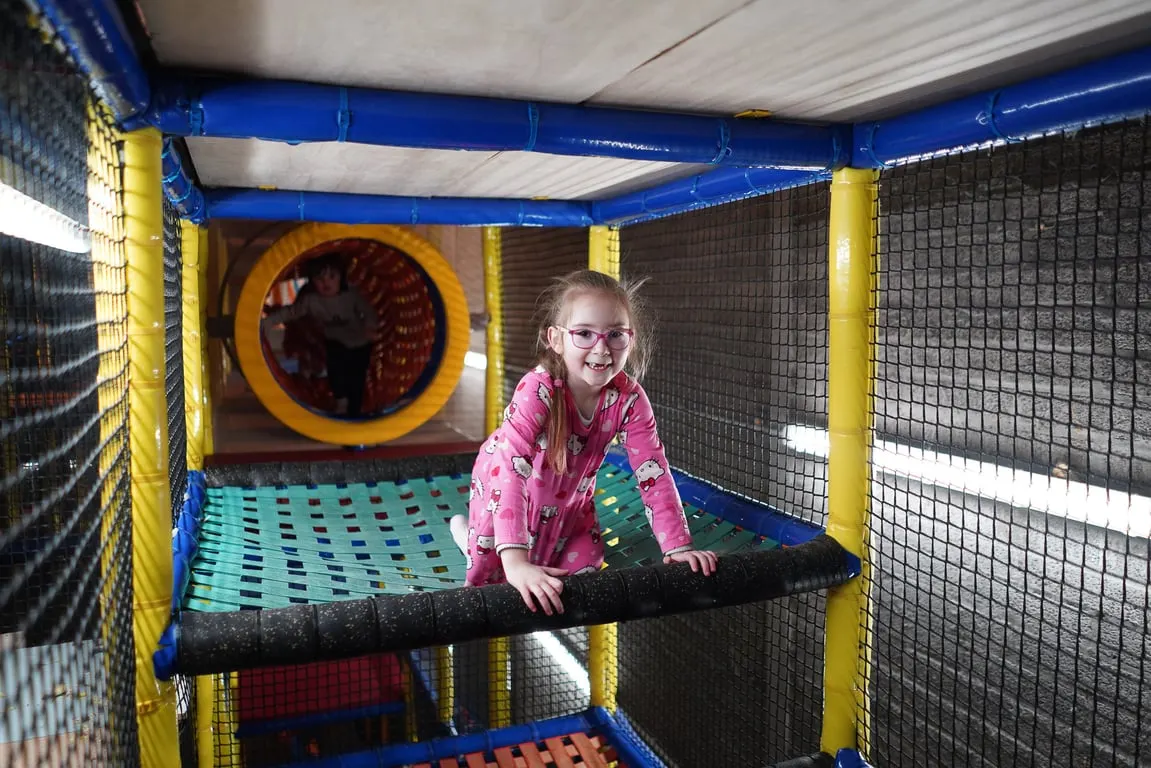 Child in pink clothing playing inside a soft play structure with tunnels and climbing features.