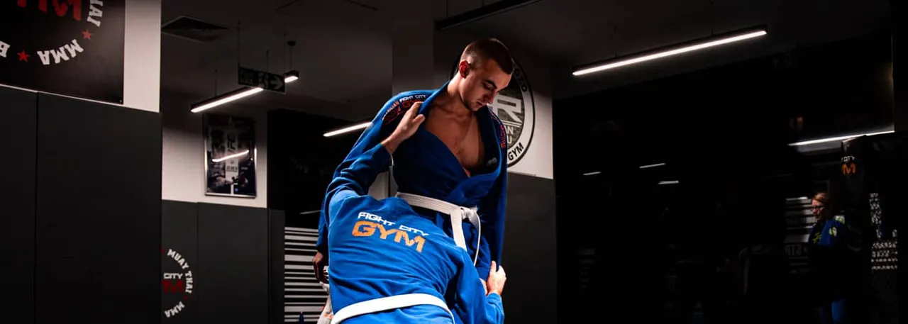 Man in blue martial arts gi adjusting his collar in a modern gym with neon lighting.