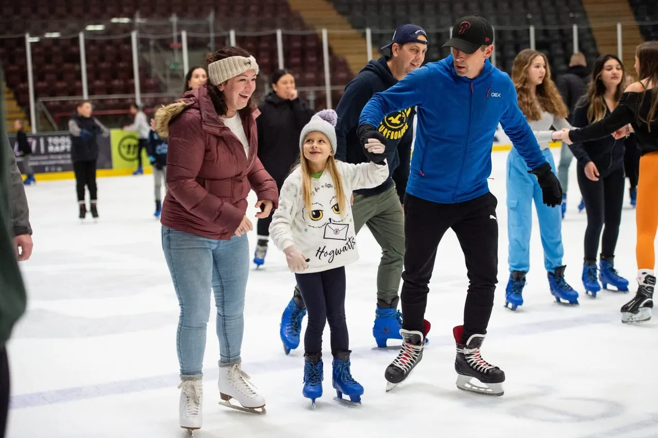 Adults and a child ice skating together on an indoor rink surrounded by other skaters.