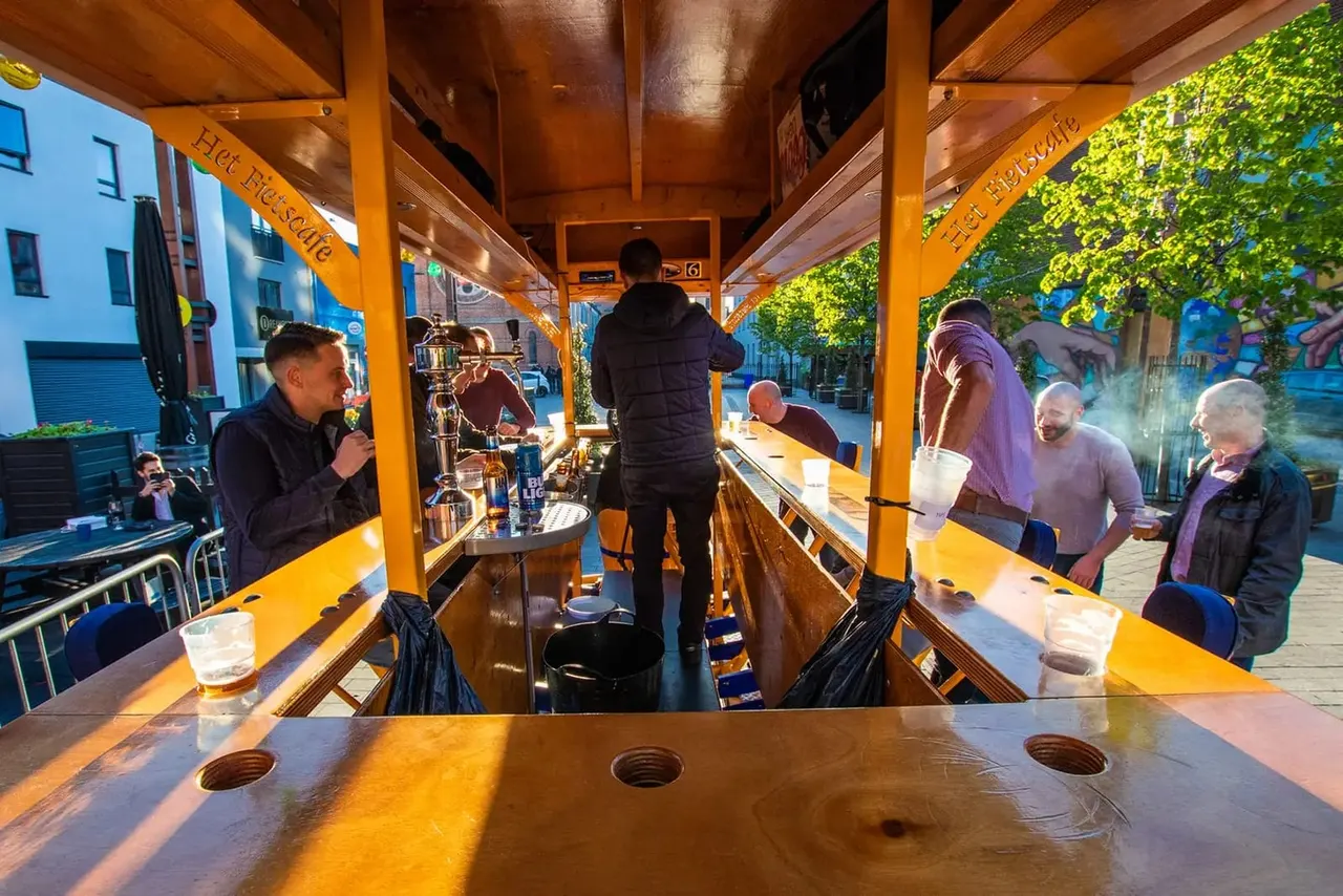 People enjoying drinks and socialising inside a yellow-roofed mobile bar on an urban street.