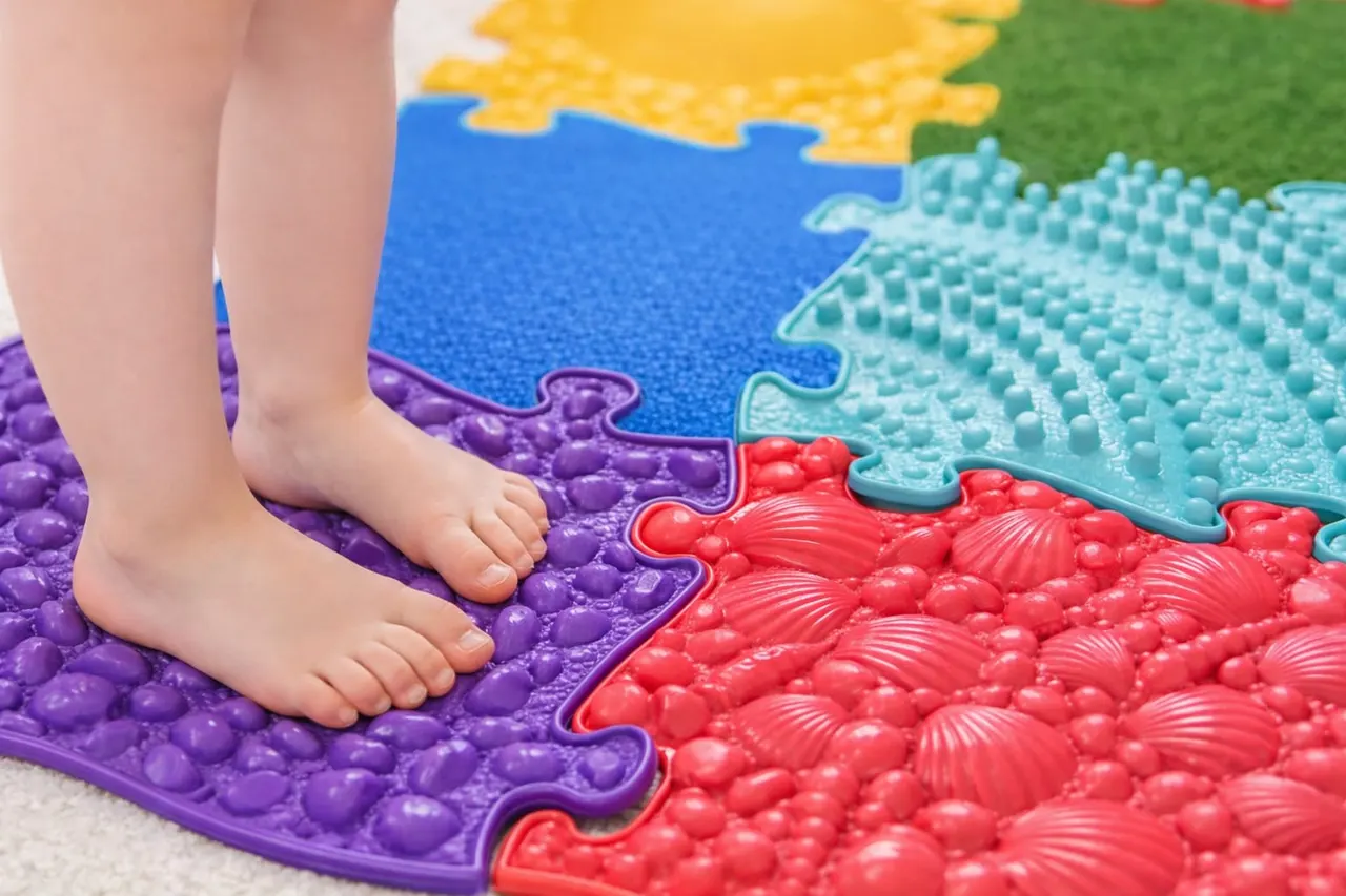 Child's bare feet on a colourful textured sensory play mat with interlocking puzzle pieces in purple, red, turquoise and yellow.