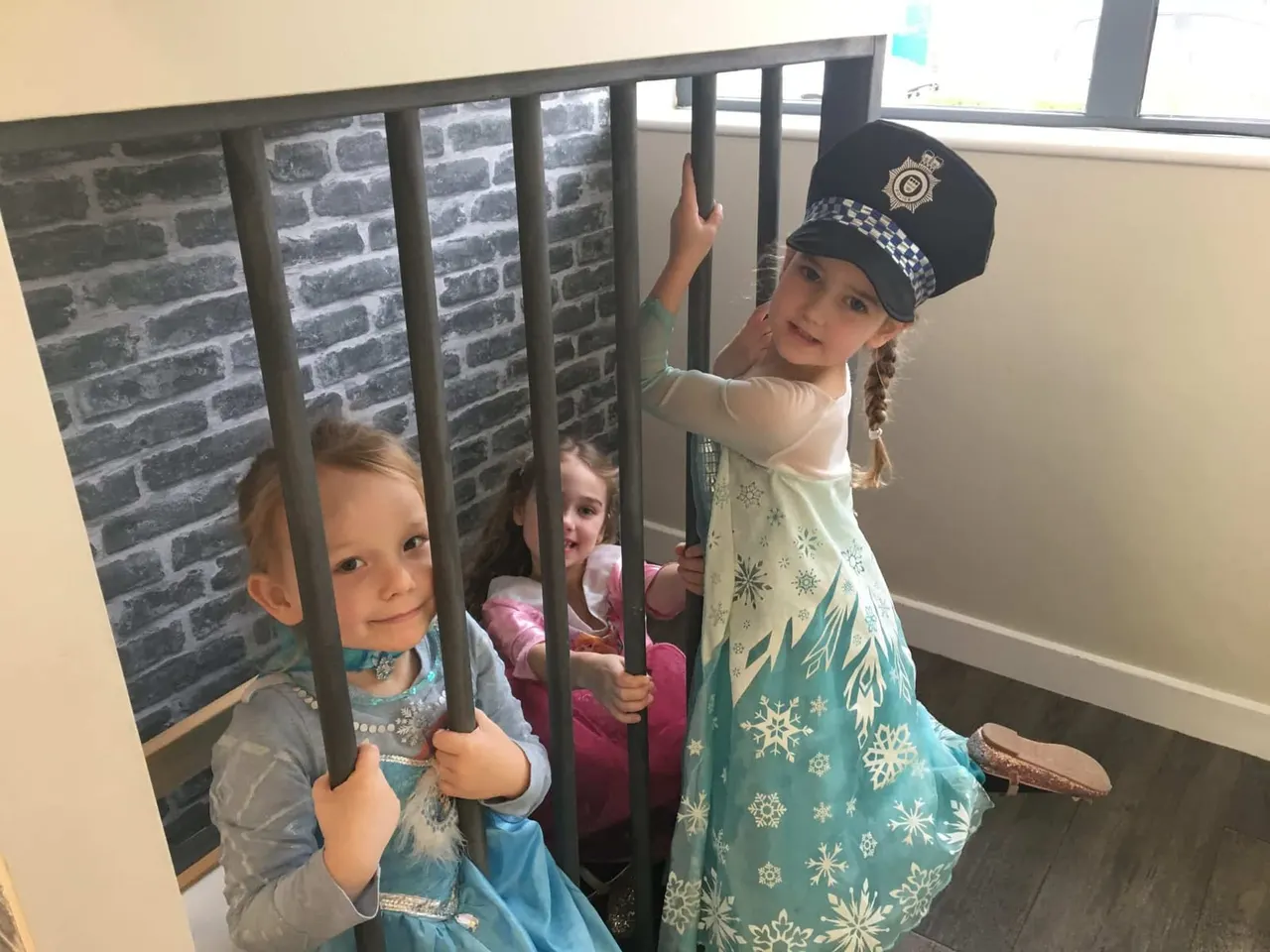 Children in fancy dress costumes playing behind a barred gate prop during an indoor activity.