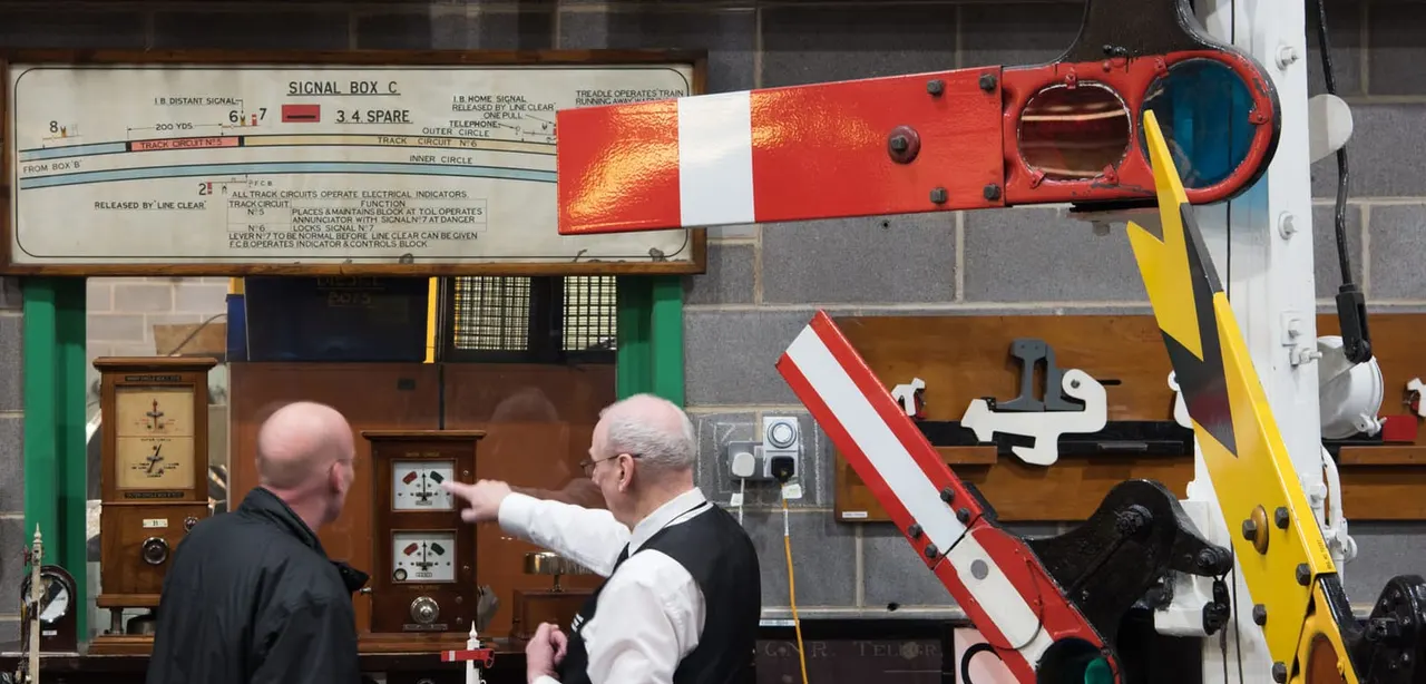 Two men examine vintage railway signalling equipment and controls displayed in a museum exhibition.